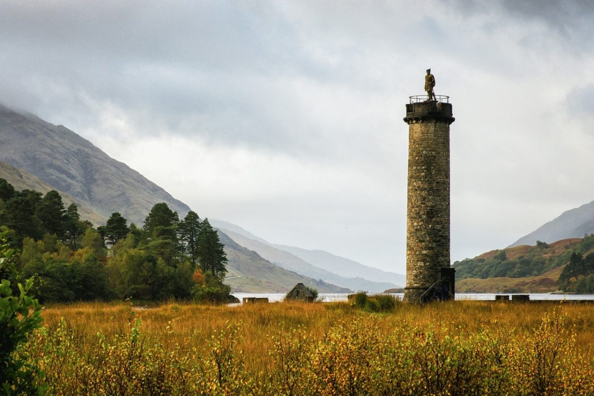 Glenfinnan-Denkmal am Ufer des Loch Shiel: Majestätische Statue eines geflügelten Highlanders auf einem hohen Steinsäulensockel, umgeben von einer malerischen Landschaft.